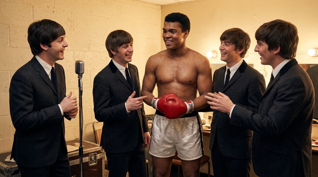 Cassius Clay torse nu avec des gants de boxe rouges entouré des quatre membres des Beatles dans leurs costumes sombres.