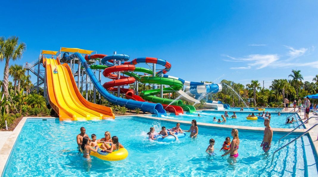 Familles et enfants s'amusant dans une grande piscine sous des toboggans aquatiques colorés par une journée ensoleillée.